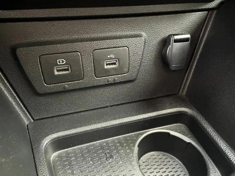 Prise USB et prise 12V noires en gros plan dans la console centrale du Dacia Duster blanc 2024.