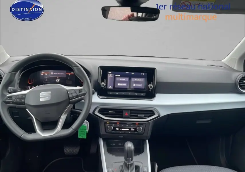 Vue intérieure frontale du tableau de bord et volant cuir noir du SEAT Arona blanc Nevada 2025 avec écran tactile central.