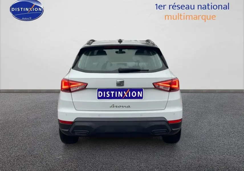 Vue arrière d'un SEAT Arona blanc Nevada avec feux allumés et logos distinctifs sur un sol gris.