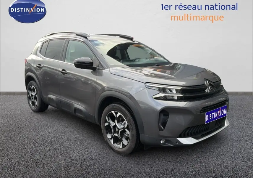 Vue 3/4 avant droite d'un Citroën C5 Aircross gris platinium métallisé avec jantes bi-ton et barres de toit.