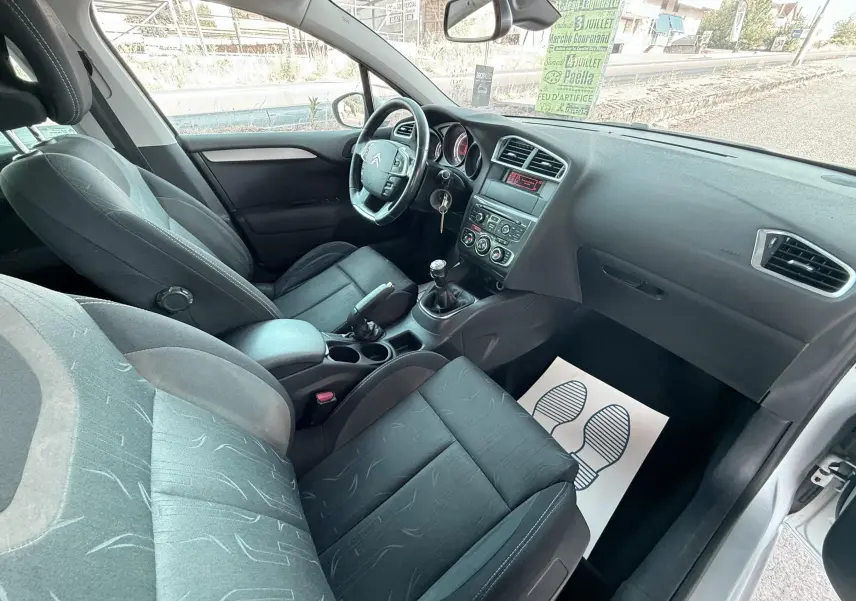 Vue intérieure côté conducteur de la Citroën C4 2011, sièges tissu noir et tableau de bord avec boîte manuelle.