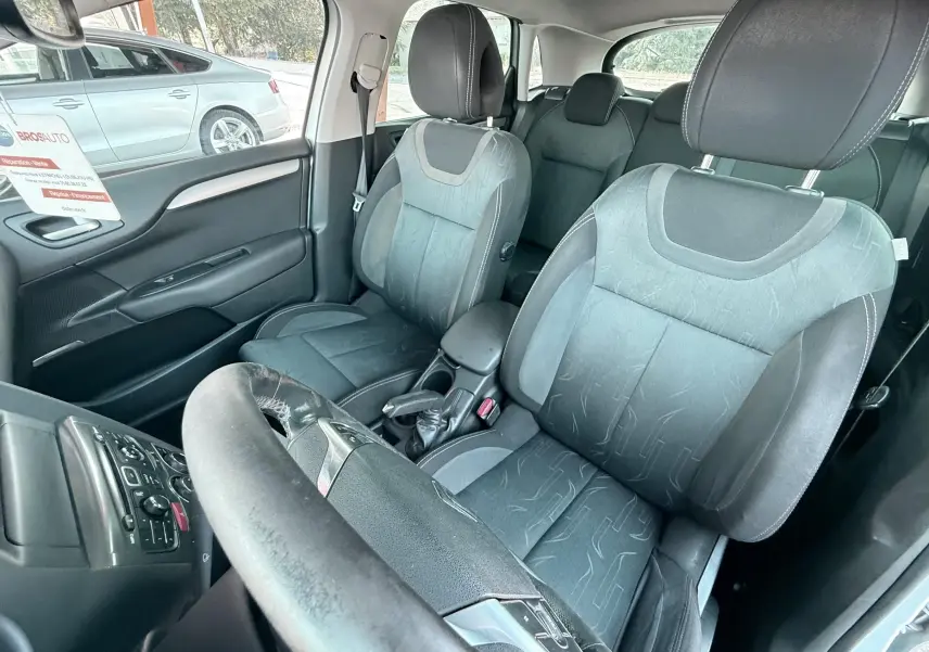 Vue intérieure côté conducteur de la Citroën C4 gris 2011 avec sièges tissu noir et volant usé.