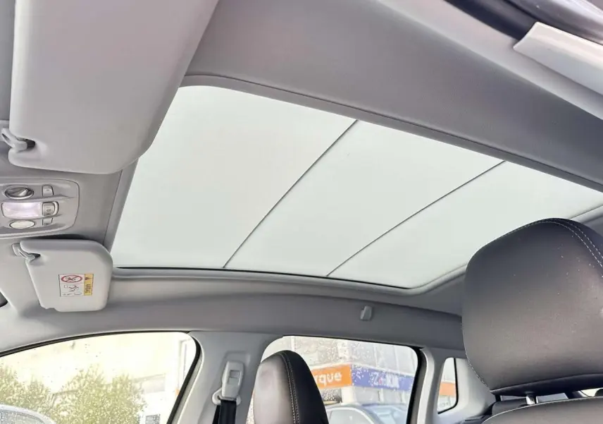 Vue intérieure du toit vitré panoramique avec velum électrique et sièges avant en cuir noir du Peugeot 2008 Crossway gris foncé.