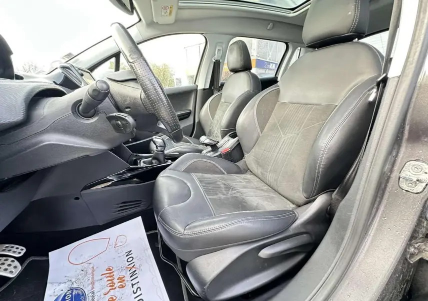 Vue intérieure côté conducteur de la Peugeot 2008 gris foncé, montrant sièges cuir et alcantara, volant et toit panoramique.
