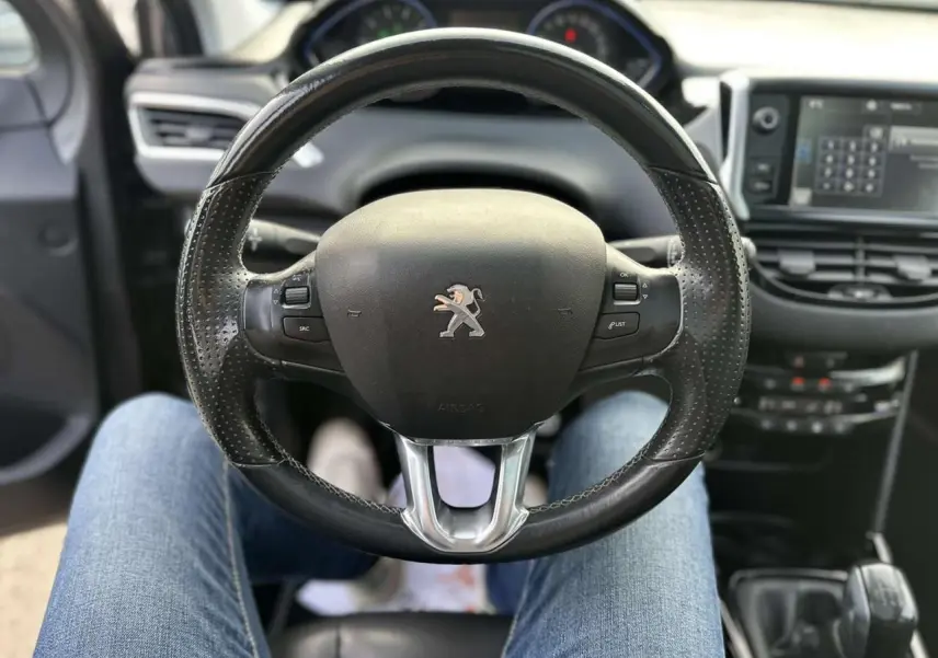 Vue intérieure centrée sur le volant cuir perforé de la Peugeot 2008 gris foncé avec tableau de bord et écran tactile.