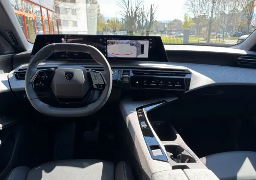 Vue intérieure avant du Peugeot 5008 Hybrid 145 Allure Plus, volant cuir multifonctions et écran panoramique 21 pouces affichant caméra 360°