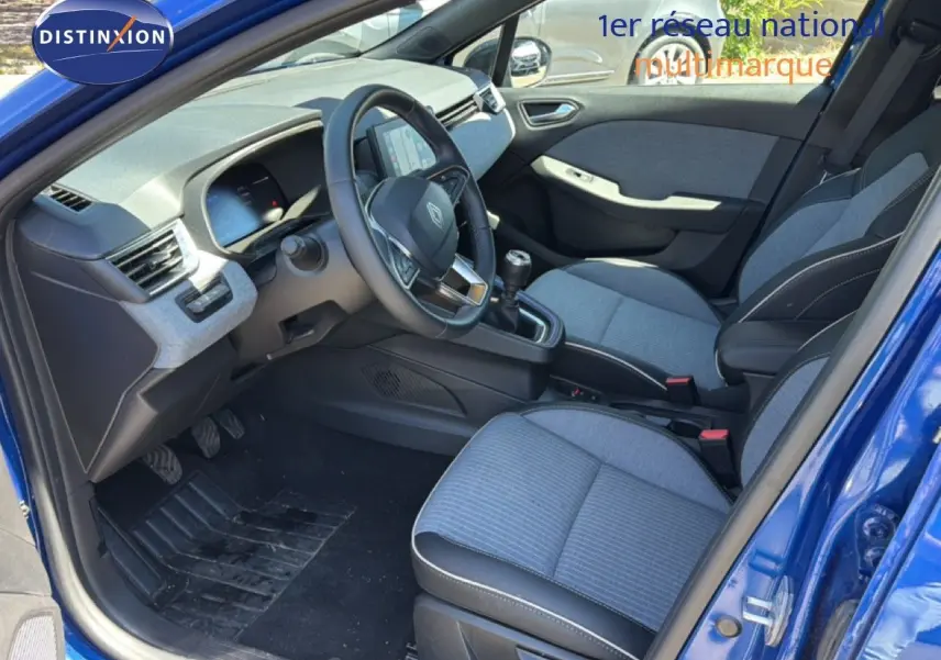 Vue intérieure côté conducteur de la Renault Clio 2025 bleu Iron Metal, avec sièges tissu gris et volant cuir multifonction.