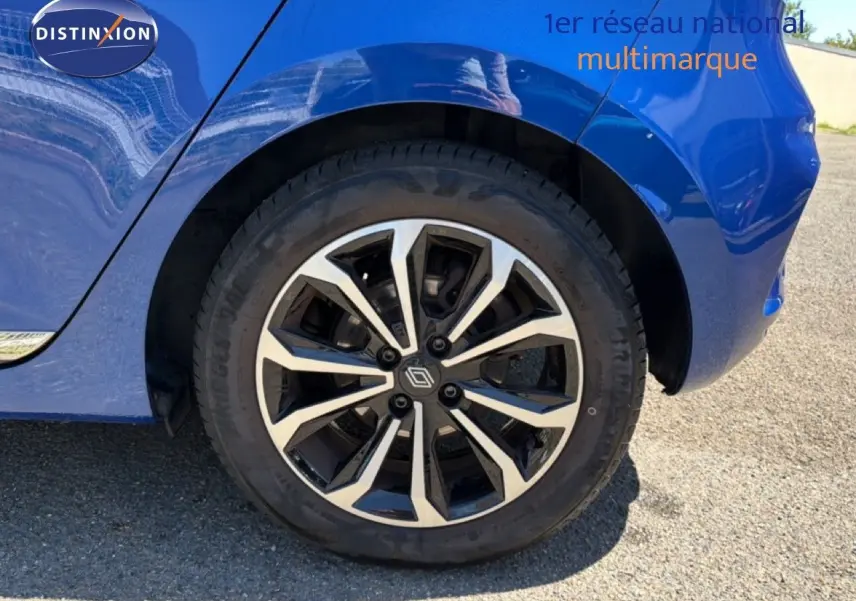 Gros plan sur la roue arrière droite d’une Renault Clio bleu iron metal avec jante alliage bicolore design moderne.