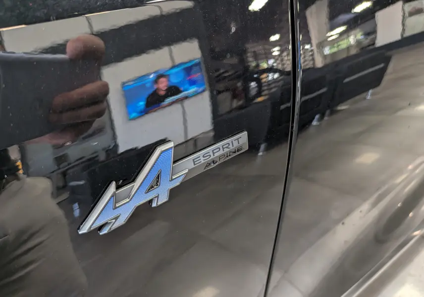 Gros plan sur l'emblème Esprit Alpine bleu et argent sur la porte noire étoilée d'une Renault Rafale.