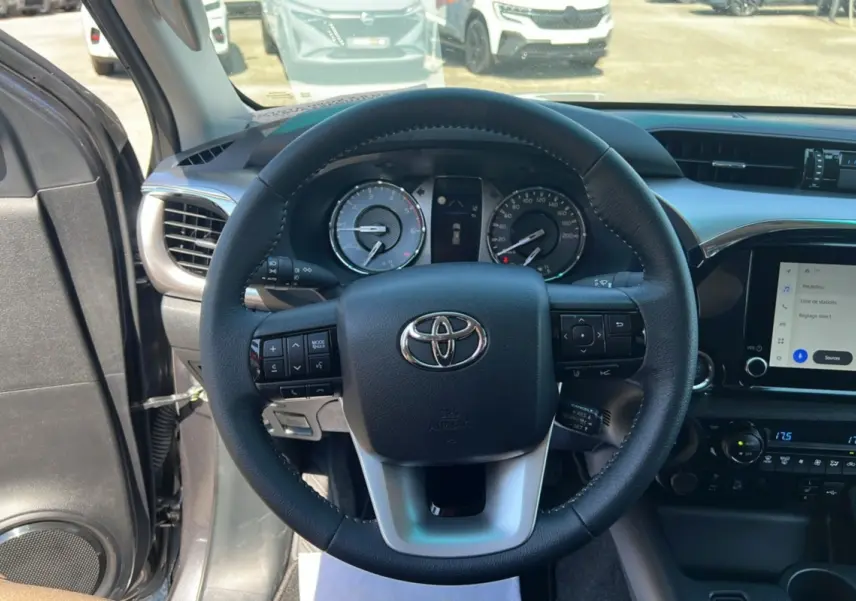 Vue intérieure centrée sur le volant cuir multifonctions du Toyota Hilux 2026, avec tableau de bord et écran tactile visibles.