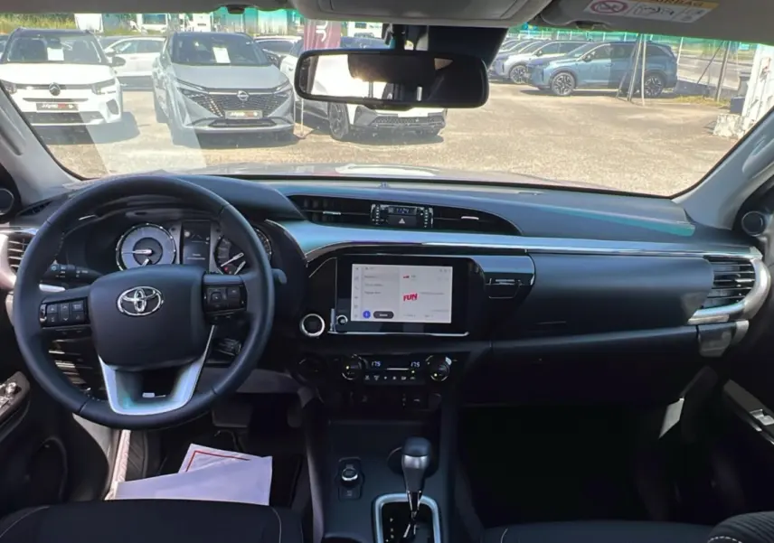 Vue intérieure du tableau de bord du Toyota Hilux 2026, avec volant multifonctions, écran tactile central et commandes de climatisation.