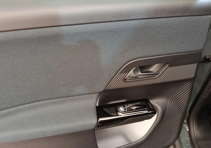 Vue intérieure côté gauche de la porte avant d’une Citroën C5 hybride 2026 avec tissu gris et insert plastique noir texturé.