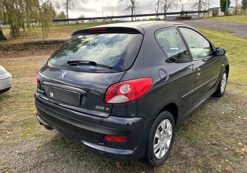 Peugeot 206+ gris foncé vue en 3/4 arrière droit, avec feux arrière rouges et jantes alliage visibles.