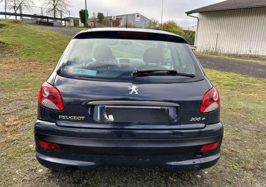 Vue arrière d'une Peugeot 206+ gris foncé de 2009 avec feux rouges et logo lion au centre du hayon.