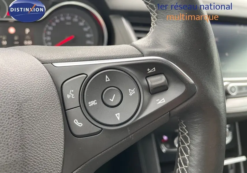 Gros plan sur les commandes au volant en cuir noir de l'Opel Grandland X Golden Sunstone, tableau de bord flou en arrière-plan.