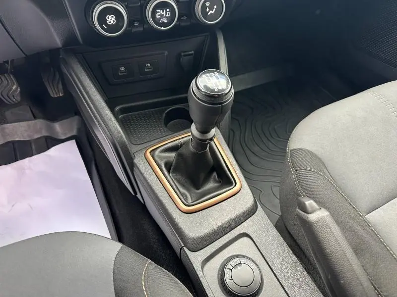 Gros plan sur la boîte manuelle et la console centrale du Dacia Duster 2024, avec sièges gris et commandes de climatisation visibles.