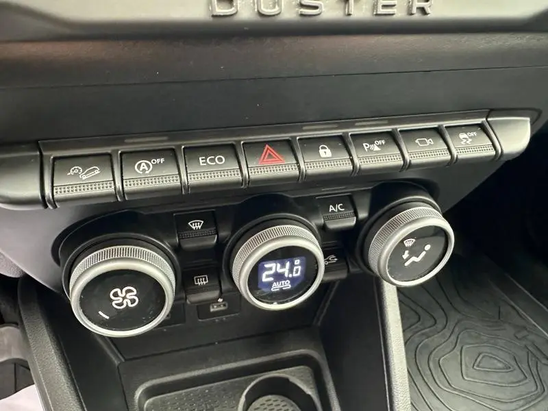 Gros plan sur la console centrale du Dacia Duster 2024 blanc, montrant les commandes de climatisation et les boutons de fonction.