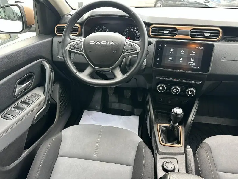Vue intérieure du tableau de bord du Dacia Duster 2024, avec volant multifonction et écran tactile central.