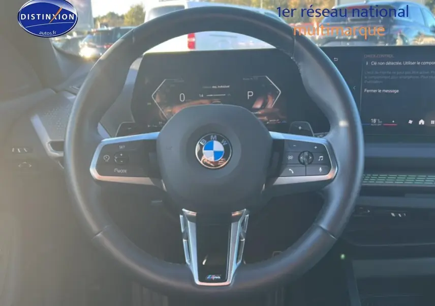Vue intérieure centrée sur le volant BMW M Sport avec commandes multifonctions et tableau de bord numérique.