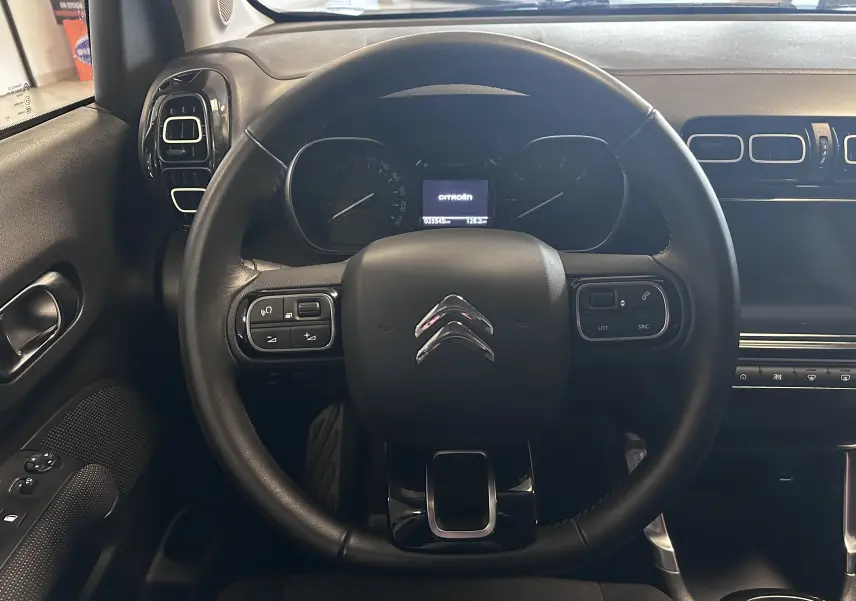Vue intérieure centrée sur le volant en croûte de cuir du Citroën C3 Aircross 2024, tableau de bord et commandes visibles.
