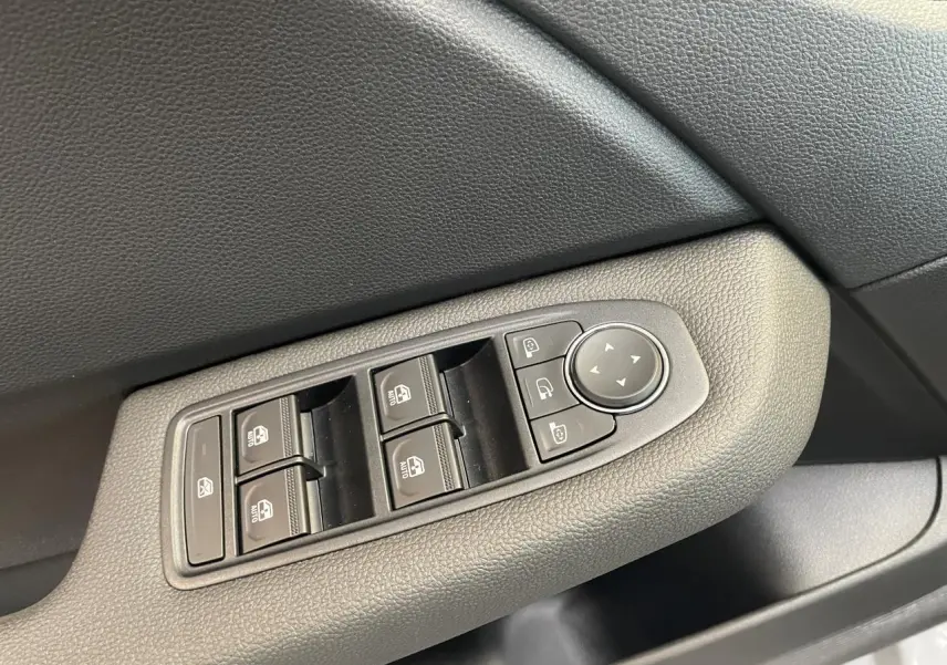 Gros plan sur les commandes des vitres électriques et rétroviseurs sur la porte côté gauche d'une Renault Clio gris Rafale.