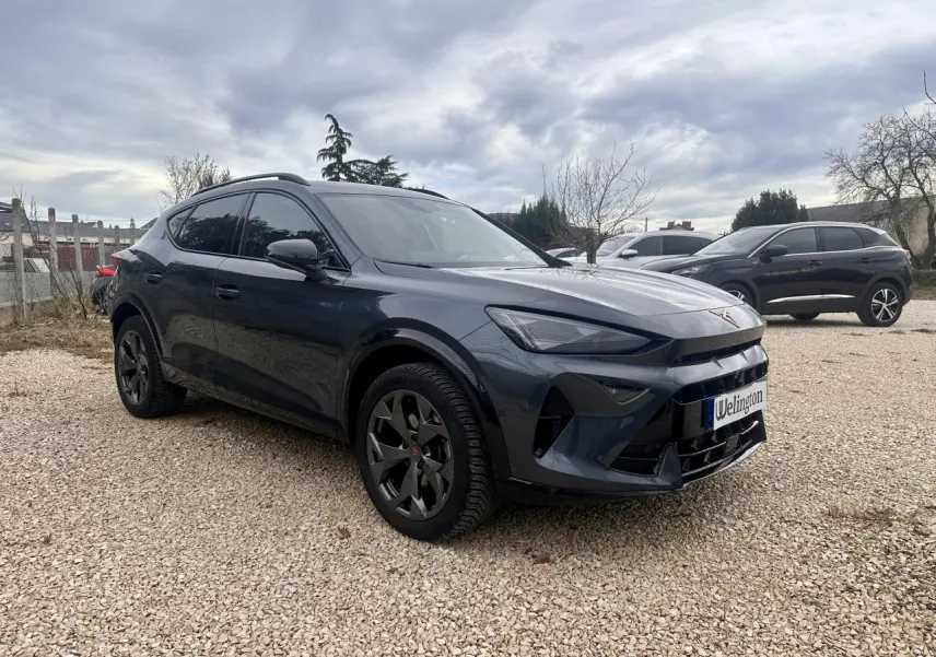 SUV CUPRA Formentor gris en 3/4 avant droit, avec jantes noires et calandre distinctive sous un ciel nuageux.