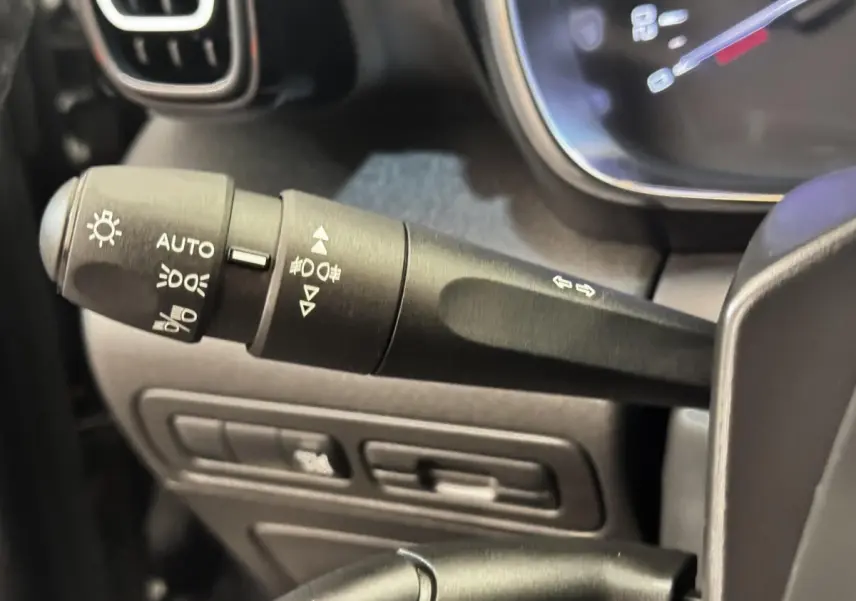 Gros plan sur la commande des phares et clignotants à gauche du volant dans une Citroën C3 gris foncé de 2019.