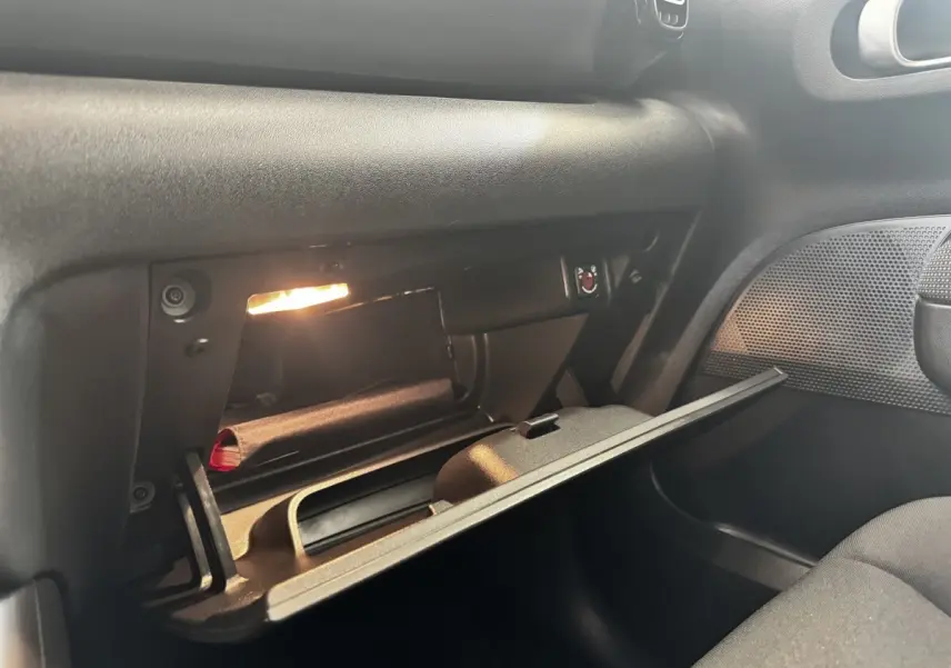 Boîte à gants ouverte côté passager de la Citroën C3 gris foncé, éclairée et montrant un rangement intérieur.