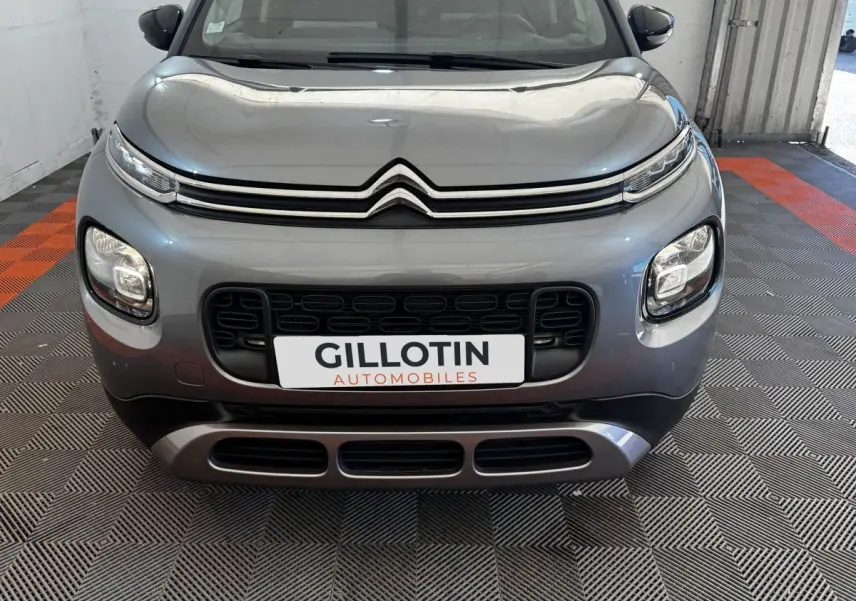 Vue avant d'une Citroën C3 gris foncé avec calandre noire et phares LED distinctifs, en intérieur showroom.