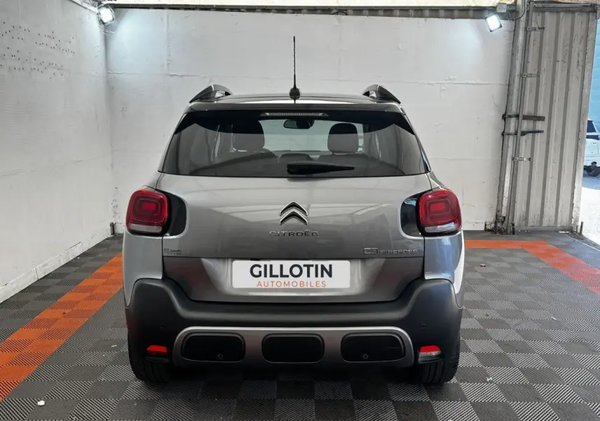 Vue arrière d'une Citroën C3 Aircross gris foncé, stationnée en intérieur sur sol à damier noir et orange.