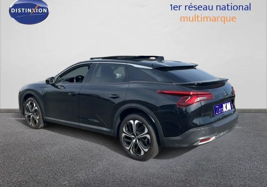 Vue 3/4 arrière gauche d'une Citroën C5 X noire métal 2023 avec jantes bi-ton et toit panoramique.