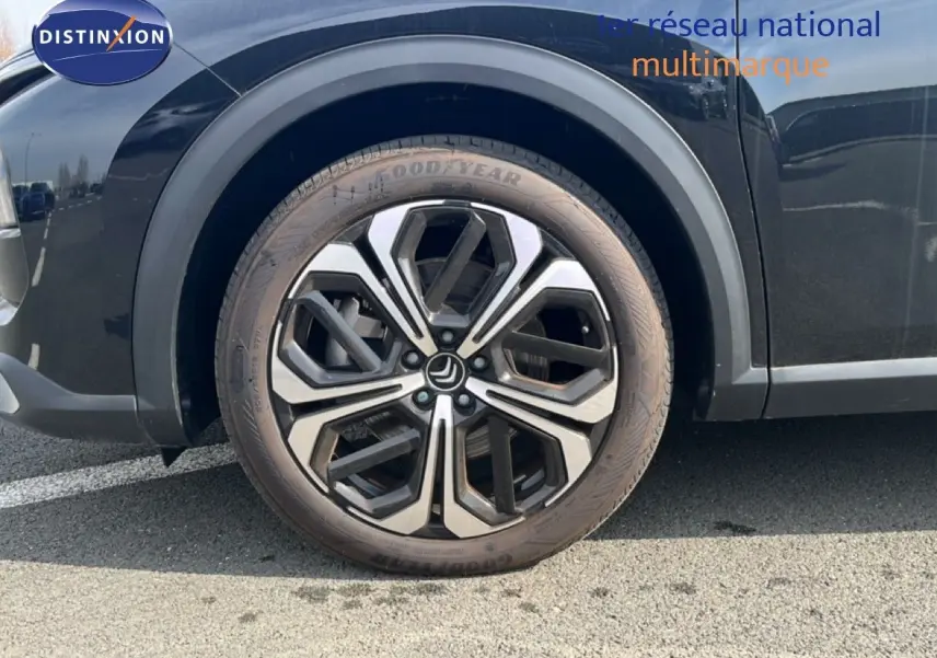 Gros plan sur la roue avant gauche d'une Citroën C5 X noire métallisée avec jante alliage bicolore.
