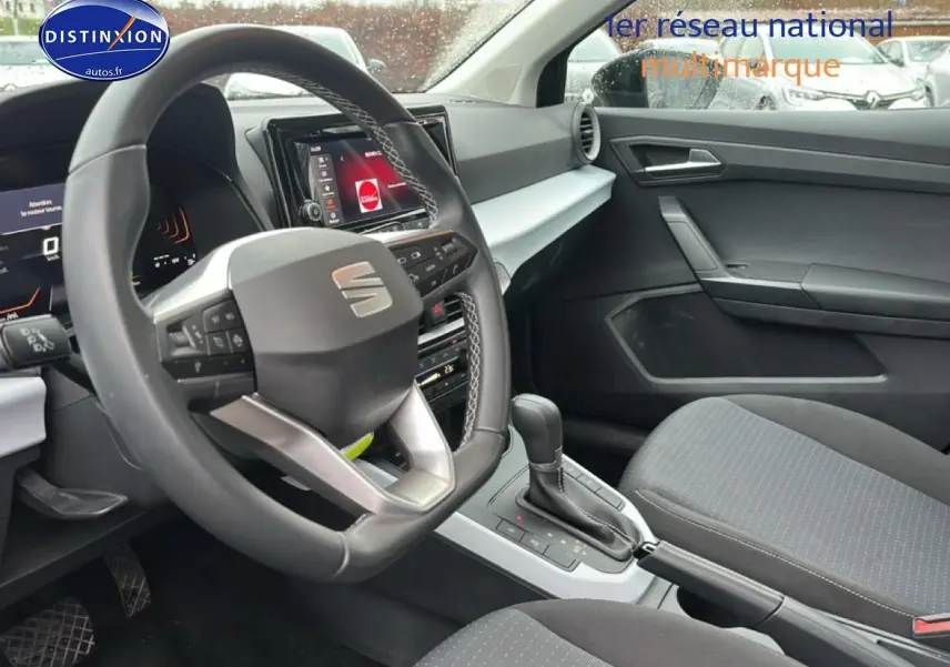 Vue intérieure côté conducteur du SEAT Arona 2025 noir minuit, volant cuir méplat et console centrale avec levier de boîte auto.