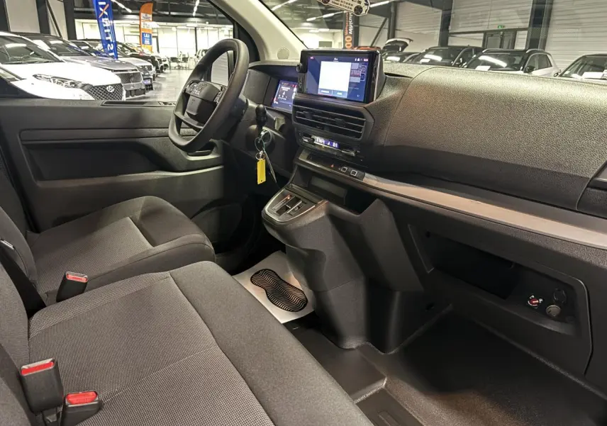 Vue intérieure côté conducteur du Fiat Scudo Fourgon gris foncé, montrant le tableau de bord moderne avec écran tactile et volant multifonction.