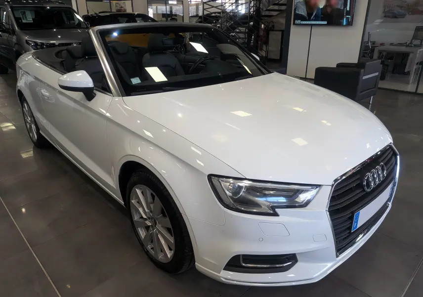 Audi A3 Cabriolet blanc vue de face avec capote ouverte, intérieur noir visible en showroom.