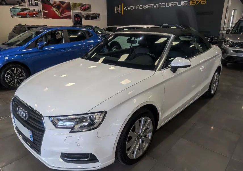 Audi A3 Cabriolet blanc vue 3/4 avant droit, capote noire fermée, dans un showroom lumineux.
