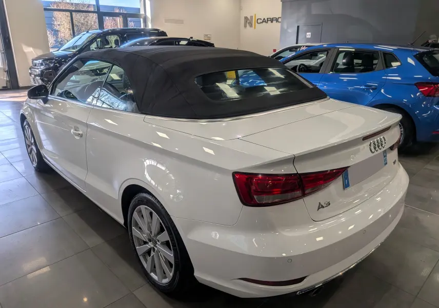 Audi A3 Cabriolet blanc vue 3/4 arrière droit avec toit souple noir dans un showroom lumineux.