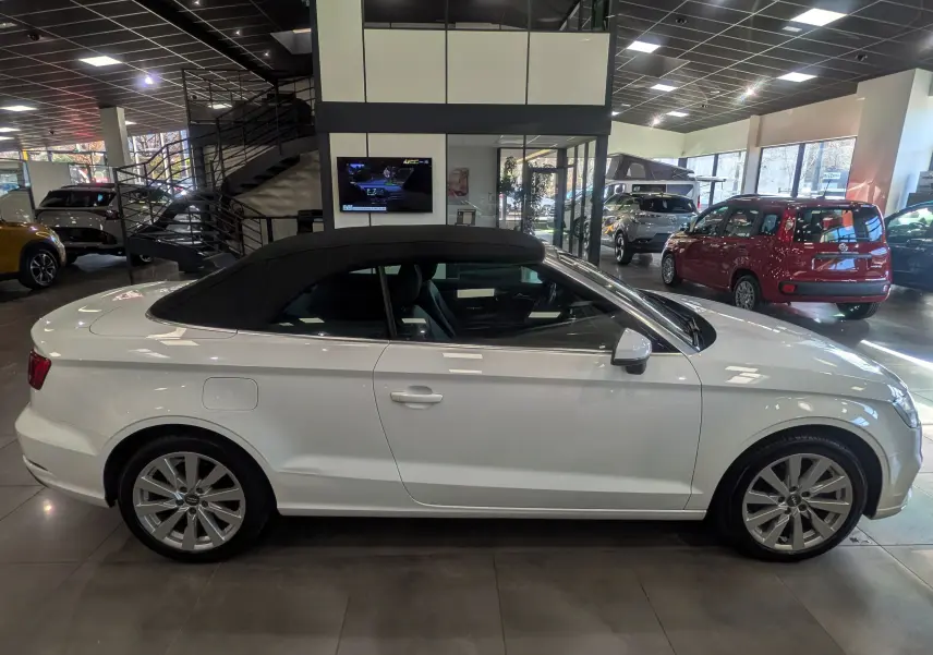 Audi A3 Cabriolet blanc vue de profil côté gauche avec toit noir fermé en intérieur showroom.