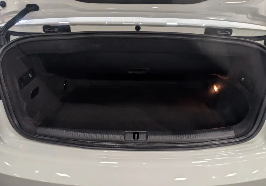 Coffre ouvert vu de face d’une Audi A3 Cabriolet blanche, intérieur noir avec éclairage latéral droit.