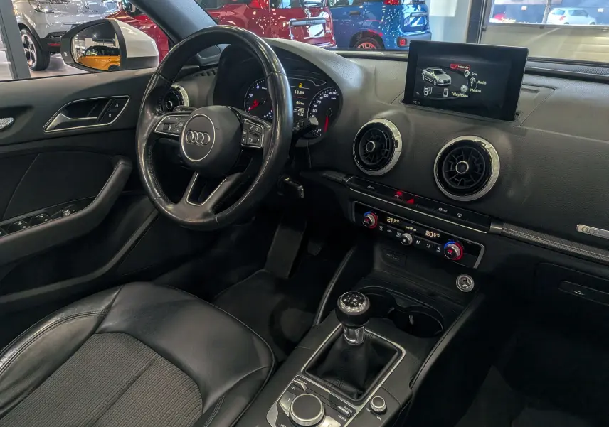 Vue intérieure côté conducteur de l'Audi A3 Cabriolet 2017, volant cuir noir, tableau de bord avec écran multimédia et boîte manuelle.