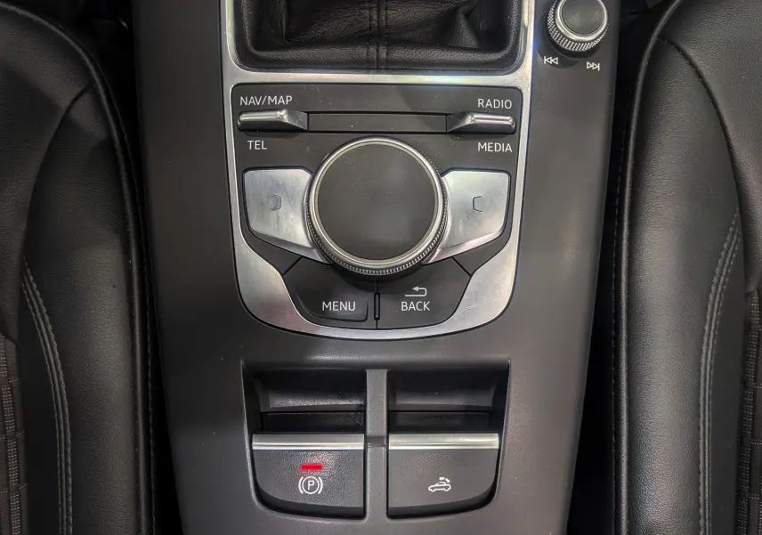 Gros plan sur la console centrale noire de l'Audi A3 Cabriolet 2017, avec commandes multimédia et boutons de frein à main et capote.