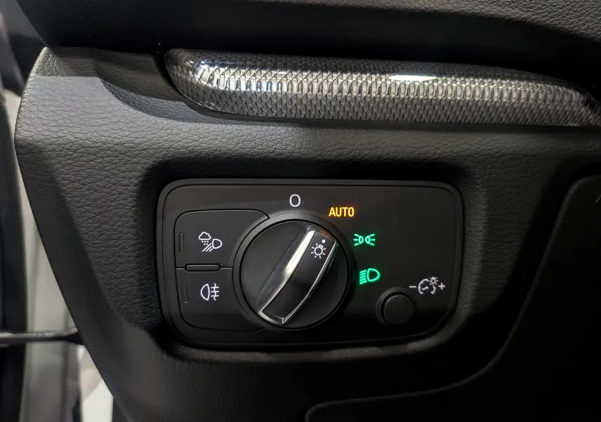 Gros plan sur le bouton de commande des phares avec réglage automatique, sur le tableau de bord noir de l'Audi A3 Cabriolet blanc.