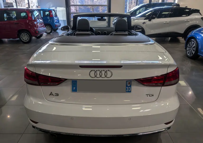 Vue arrière d'une Audi A3 Cabriolet blanche 2017 avec capote rabattue, dans un showroom lumineux.