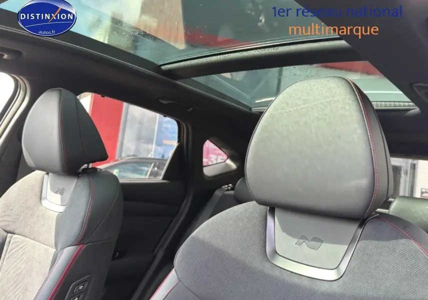 Vue intérieure du Hyundai Tucson noir 2026, sièges avant en cuir et alcantara avec surpiqûres rouges et toit panoramique en verre.