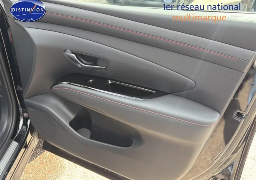 Gros plan sur la porte avant gauche noire du Hyundai Tucson 2026 avec surpiqûres rouges et poignée chromée.