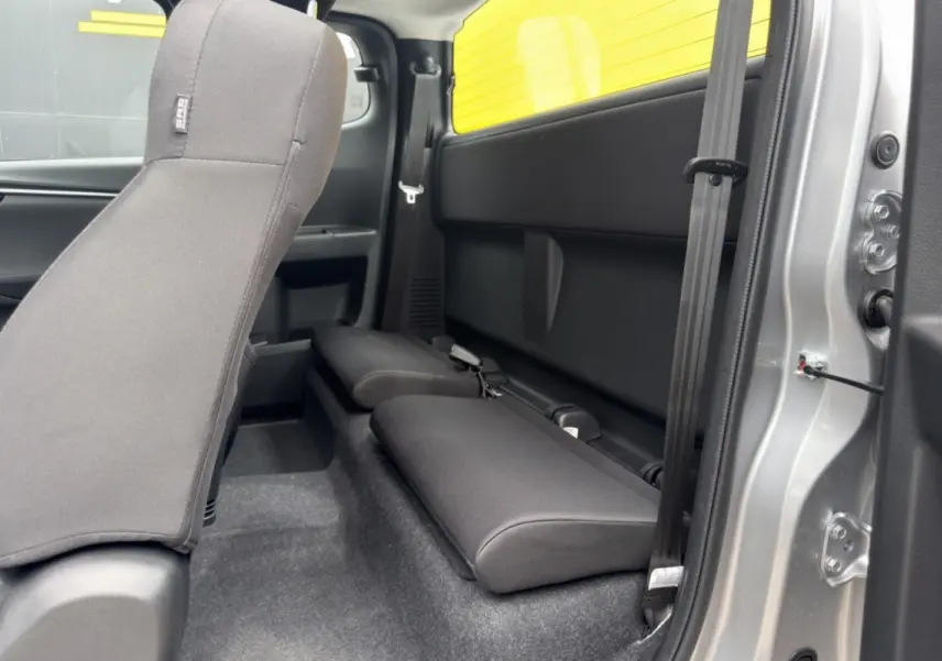 Vue intérieure côté droit du pick-up Isuzu D-MAX 2026, sièges arrière strapontins en tissu noir, carrosserie argentée visible.