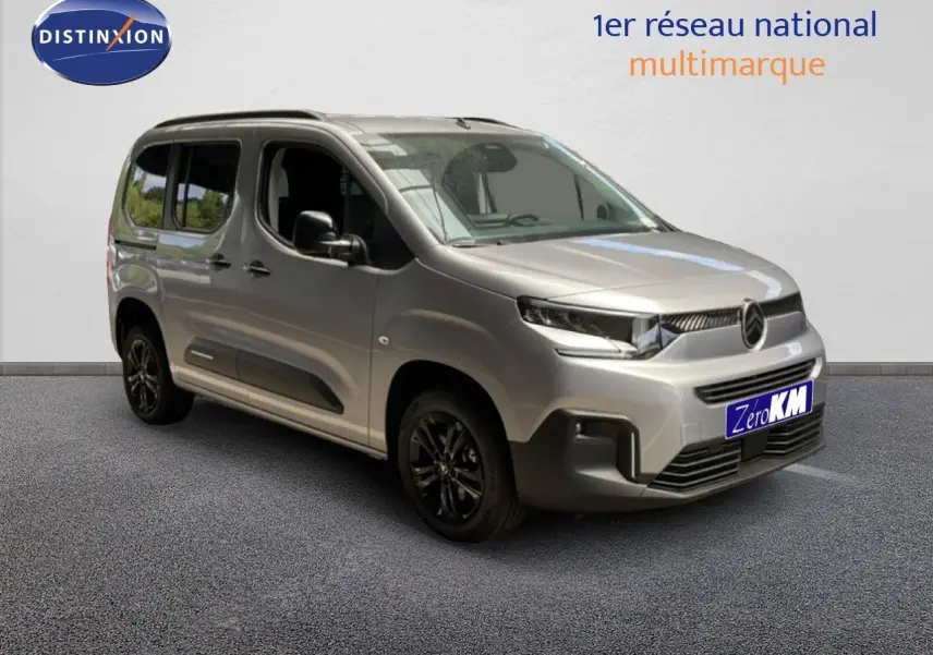 Vue 3/4 avant d'un Citroën Berlingo gris Artense métal avec jantes noires, présenté en intérieur showroom.