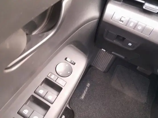Détail intérieur côté conducteur du Hyundai Kona 2024, montrant les commandes des vitres et le tapis noir marqué Hyundai.