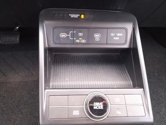 Vue rapprochée de la console centrale noire du Hyundai Kona 2024, avec bouton Drive Mode et prises USB et 12V visibles.