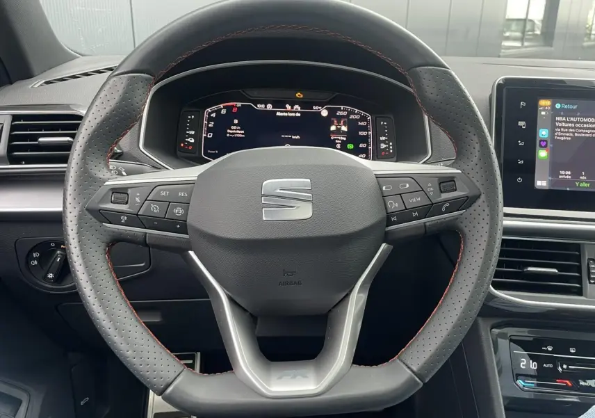 Volant sport en cuir avec surpiqûres rouges et tableau de bord numérique du SEAT Tarraco FR gris dauphin, vue de face intérieure.